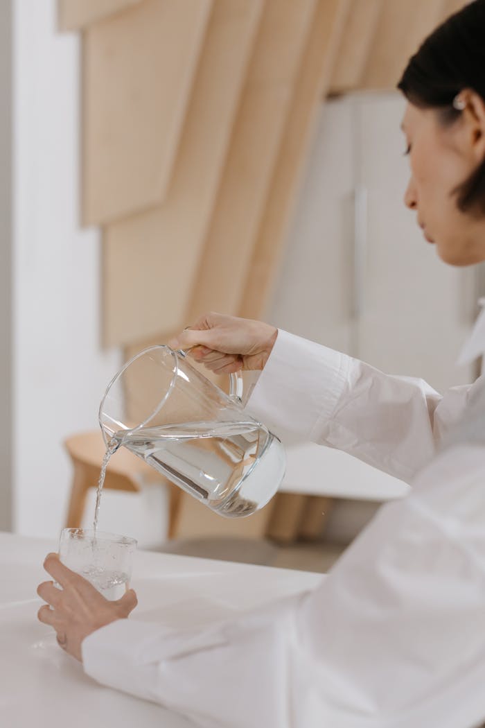 Woman in white shirt pouring water from a pitcher into a glass in a modern indoor setting.